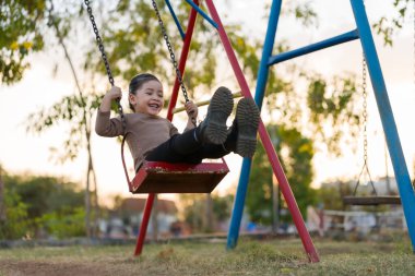 Neşeli kız çocuk parkta salıncakta oynuyor.