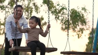 Annesiyle birlikte çocuk parkında salıncakta sallanan neşeli kızın ağır çekimleri.