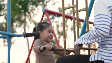 Annesiyle açık hava çocuk parkında çifte salıncakta oynayan neşeli kızın ağır çekimleri.