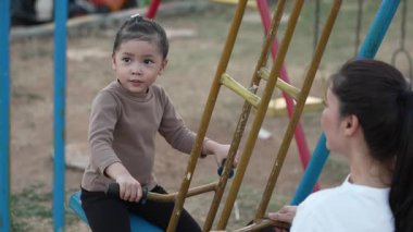 Annesiyle açık hava çocuk parkında çifte salıncakta oynayan neşeli kızın ağır çekimleri.