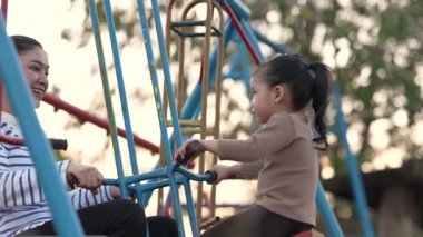 Annesiyle açık hava çocuk parkında çifte salıncakta oynayan neşeli kızın ağır çekimleri.