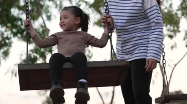 Annesiyle birlikte çocuk parkında salıncakta sallanan neşeli kızın ağır çekimleri.