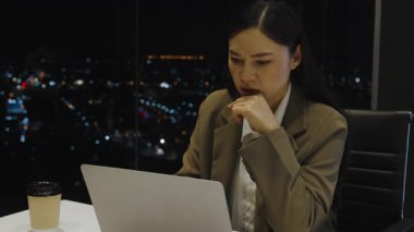 İş kadını, geceleri şehrin ışıklarıyla donatılmış yüksek katlı iş yerlerinde dizüstü bilgisayarla çalışırken düşünüyor.