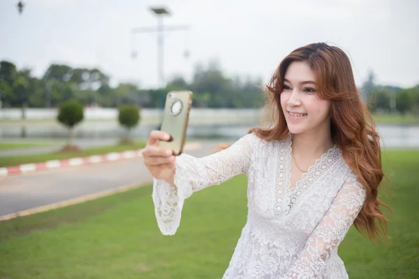 Mooie jonge vrouw selfie in het park met een smartphone — Stockfoto