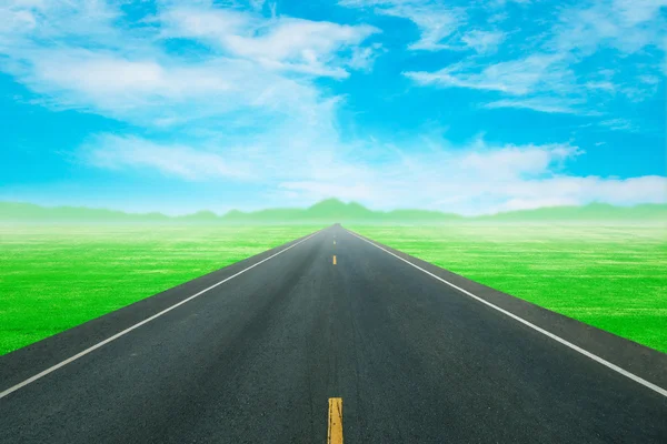 Асфальтовая дорога через зеленое поле с небом — стоковое фото