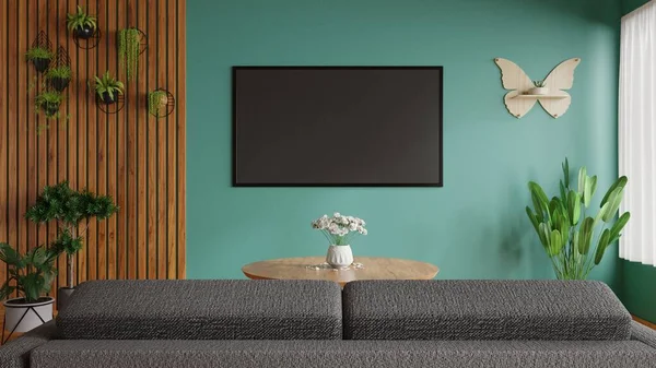 Televizyon odasının yanında dekoratif bir bitki, önünde bir kanepe ve güzel yeşil bir duvar 3D çerçeveli büyük bir televizyon var.