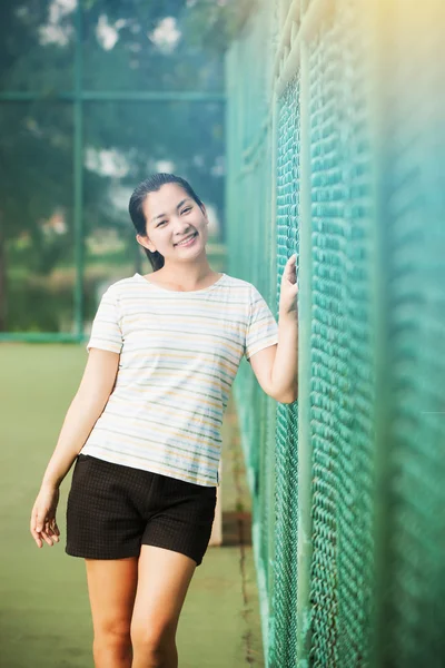 亚洲女性放松和微笑站在网球场上 — 图库照片