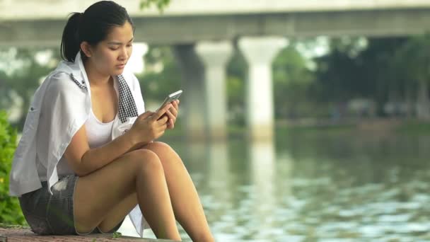 Young asian woman using smartphone and look like relaxing in outdoors looking happy and smiling:Full HD — Stock Video