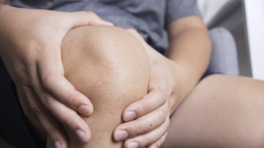 Sürekli ağrıdan muzdarip olan biri masajla ellerini dizinin üstüne koyuyor.