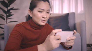 Kırmızı gömlekli Asyalı kadınlar online oyun oynamak için akıllı telefon kullanıyorlar oturma odasında heyecanlı duygular var.