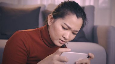 Kırmızı gömlekli Asyalı kadınlar online oyun oynamak için akıllı telefon kullanıyorlar oturma odasında heyecanlı duygular var.