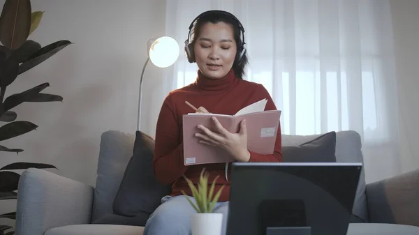 Asian woman on redshirt using a tablet with headphone for meeting online at home in coronavirus situation new normal work from home