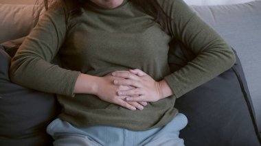 Bilinmeyen sebeplerden dolayı karın ağrısı ve karın ağrısı olan kadın oturma odasındaki kanepede yatıyor..