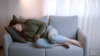 Bilinmeyen sebeplerden dolayı karın ağrısı ve karın ağrısı olan kadın oturma odasındaki kanepede yatıyor..