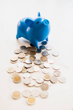 Mavi domuz kumbarası, içi bozuk para dolu bir masaya yerleştirilmiş. Yumuşak ışıklar ve fotokopi alanı ile saçılmış. Para tasarruf kavramı