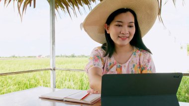 Evinin önünde dijital tabletiyle çalışan Asyalı bir kadın. Arka plandaki pirinç tarlasında.