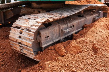 Kazıcının pistinin yakın plan görüntüsü toprak içinde gömülü. İnşaat alanında ağır makineler çalışıyor..