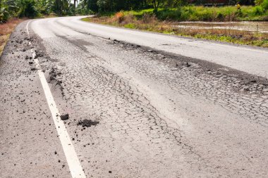 image showcases a damaged roadway with severe cracks and debris highlighting infrastructure issues in a rural setting.