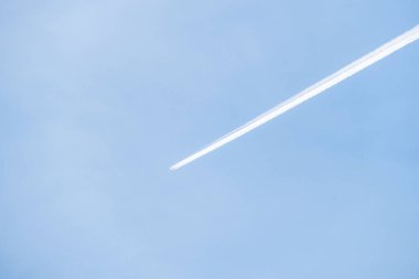 Bir uçak, gökyüzünün durgun ve mavi rengine karşı belirgin bir iz bırakır .