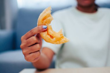 Yarısı yenmiş bir çöreği tutan bir elin yakın plan çekimi tatlı bir ziyafetin tadını çıkarıyor..