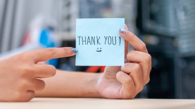 Sıradan bir ofiste minnettarlığı vurgulayan bir teşekkür notu tutan bir elin yakın çekimi..