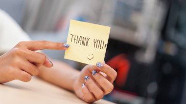 Ofiste bir teşekkür notu tutan bir elin parlak bir atmosferde minnettarlığını ifade ettiği yakın plan görüntüsü..