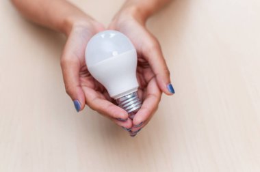 Elde tutulan yaratıcı ampul, ev ışıklandırmasındaki yeniliği ve sürdürülebilirliği simgeler..