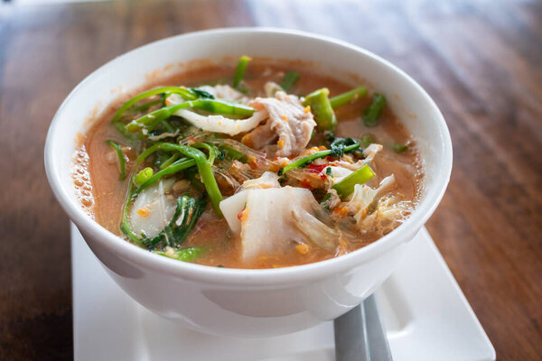 Яркая миска острого супа с лапшой, украшенная свежими травами, демонстрирующими местные вкусы.