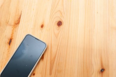 Akıllı telefon, kapalı bir ortamda minimalist bir tasarımın altını çizen doğal bir ahşap yüzeyi barındırır..
