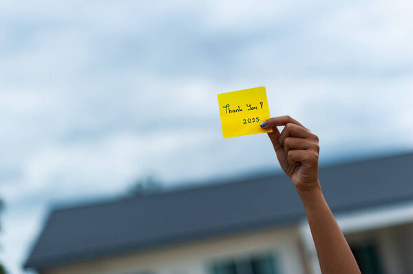 Рука держит благодарственную записку на собрании сообщества, выражая благодарность в непринужденной обстановке на открытом воздухе.