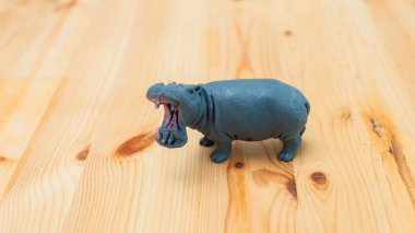 Eğlenceli bir plastik hipopotam oyuncağı yumuşak ahşap bir masa esnerken canlı renkler ve oyuncu tasarım sergiliyor..