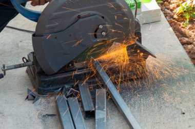 Bir işçi, atölyede kıvılcım yaratan bir testereyle metal keser..