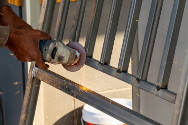 Bir işçi, endüstriyel bir atölyede ustalıkla metal bir çerçeve öğütüyor..