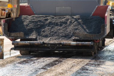Ağır bir makine titizlikle asfalt döşemiş. Şehir ortamında endüstriyel çalışmalar sergiliyor..