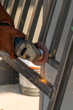 Bir zanaatkar metal öğütüyor ve hareketli bir inşaat alanında kıvılcımlar saçıyor..