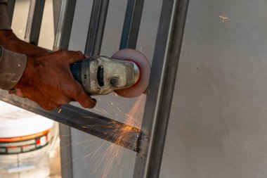 Bir zanaatkar, endüstriyel atölye ortamında kıvılcımlar saçan metal bir çerçeve öğütüyor.