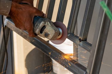 Yetenekli bir işçi, endüstriyel aletlerle dolu bir atölyede kıvılcımlar saçarak metal öğütüyor..