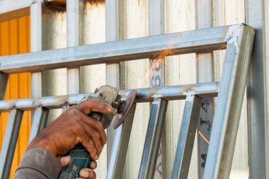 Yetenekli bir işçi, endüstriyel bir ortamda metal çerçeve işçiliğini kesmek için bir araç kullanır..