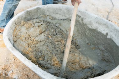 Bir işçi, temel inşaat uygulamalarını gösteren bir inşaat sahasındaki karıştırma küvetinde taze beton karıştırıyor..