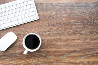 Ahşap ofis masasında bilgisayar faresi, klavye ve bir fincan kahve. Kopyalama alanı olan üst görünüm, düz yatay.