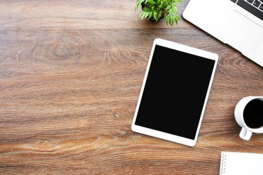 Boş ekranlı büyük tablet ahşap ofis masasının üstünde malzemelerle birlikte. Kopyalama alanı olan üst görünüm, düz yatay.