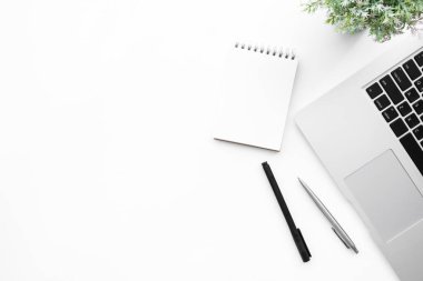 Kalem ve dizüstü bilgisayarlı boş defter sayfası olan beyaz ofis masası. Kopyalama alanı olan üst görünüm, düz yatay.