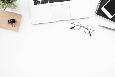 Laptop bilgisayarı, akıllı telefon ve malzemeleri olan beyaz ofis masası. Kopyalama alanı olan üst görünüm, düz yatay.