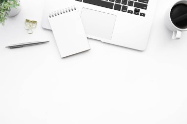 Laptop bilgisayarının üzerinde boş küçük defter sayfası olan beyaz ofis masası. Kopya alanı ve düz yatağı olan üst görünüm.