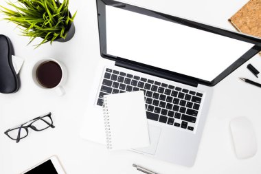 Beyaz, boş, beyaz ekranlı bir bilgisayar kahve fincanı ve malzemelerle beyaz ofis masasının üstünde. Kopyalama alanı olan üst görünüm, düz yatay.