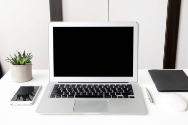 Laptop bilgisayar ve akıllı telefon beyaz ofis masasının üstünde boş maket ekranlar var..