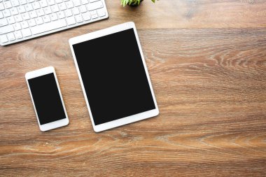Beyaz akıllı telefon ve boş sahte ekranlı masa ahşap ofis masasının üstünde bilgisayar klavyeli. Kopyalama alanı olan üst görünüm, düz yatay.