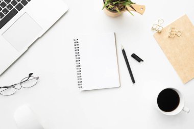 Boş defter sayfası beyaz ofis masasının üstünde malzemelerle birlikte. Üst manzara, düz uzanma.