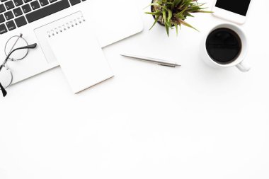 Boş not defteri dizüstü bilgisayarın üstünde beyaz ofis masasının üzerinde malzemelerle birlikte. Kopyalama alanı olan üst görünüm, düz yatay.