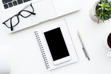 Beyaz akıllı telefon, beyaz ofis masasının üstünde malzemelerle birlikte. Kopyalama alanı olan üst görünüm, düz yatay.